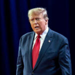 Disgraced Rapper BEGS Trump For Pardon Man in suit with red tie speaking on stage.