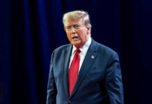 Disgraced Rapper BEGS Trump For Pardon Man in suit with red tie speaking on stage.
