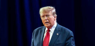 Disgraced Rapper BEGS Trump For Pardon Man in suit with red tie speaking on stage.