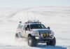 Lifted white expedition truck driving through snowy terrain