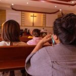 people seated in church pews facing a cross