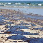 Mystery Orbs Found Scattered Across Beach Oil spill on a sandy beach with waves in the background