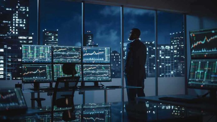 Trader in a dark office with multiple stock monitors and city skyline at night