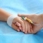 Gay Couple Abused, KILLED Adopted Child! Two hands holding, one with medical IV attached.