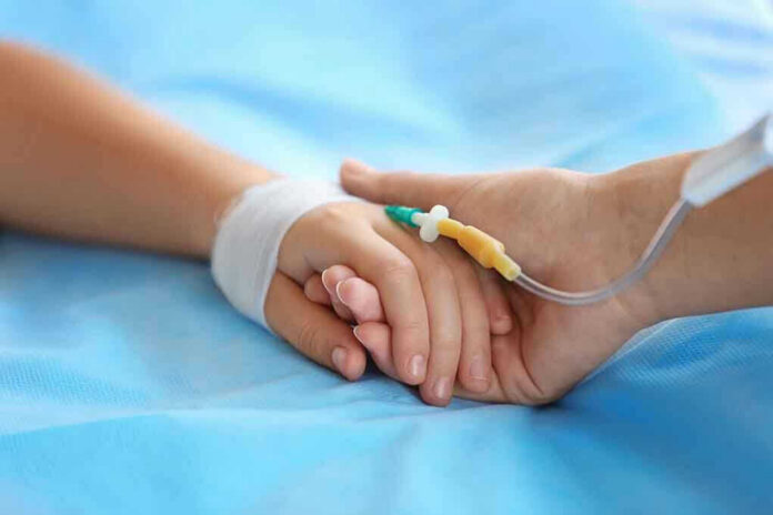 Two hands holding, one with medical IV attached.