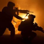 Marines Dangle $15K Bonuses For Code Warriors Two armed soldiers silhouetted against fiery smoke