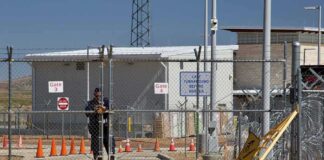Security guard at chain-link gate of fenced facility