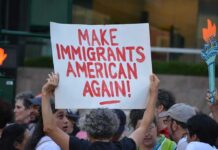 Teddy Williams at a protest holding a sign reading 'Make Immigrants American Again'