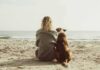 Person and dog sitting on a beach facing the sea