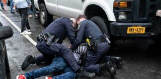 Police officers restraining a person on a wet city street beside a truck