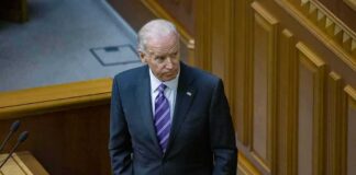 Joe Biden standing in a wood-paneled chamber in a dark suit