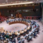 Delegates seated around a circular conference table in a large chamber