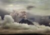 Volcano erupting with ash plume above cloud layer
