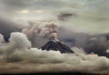 Volcano erupting with ash plume above cloud layer