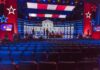 Mike Rogers Ripped El-Sayed to Shreds in CAGEY Debate Debate stage with red and blue lighting and empty audience seats