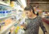 Woman shopping in dairy aisle reading a yogurt container