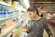 Woman shopping in dairy aisle reading a yogurt container