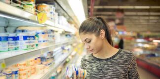 Woman shopping in dairy aisle reading a yogurt container