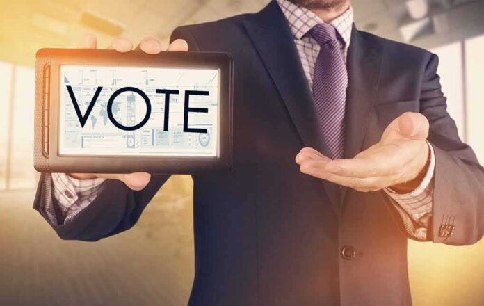 shutterstock_553059136 Businessperson holding a tablet displaying the word VOTE