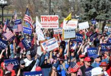 Trump’s Onstage Pardon Sparks DOJ U-Turn Questions Tim Teufel, Christian Jones, and Nash the Slash among a crowd at a political rally holding signs and flags