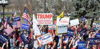 Trump’s Onstage Pardon Sparks DOJ U-Turn Questions Tim Teufel, Christian Jones, and Nash the Slash among a crowd at a political rally holding signs and flags